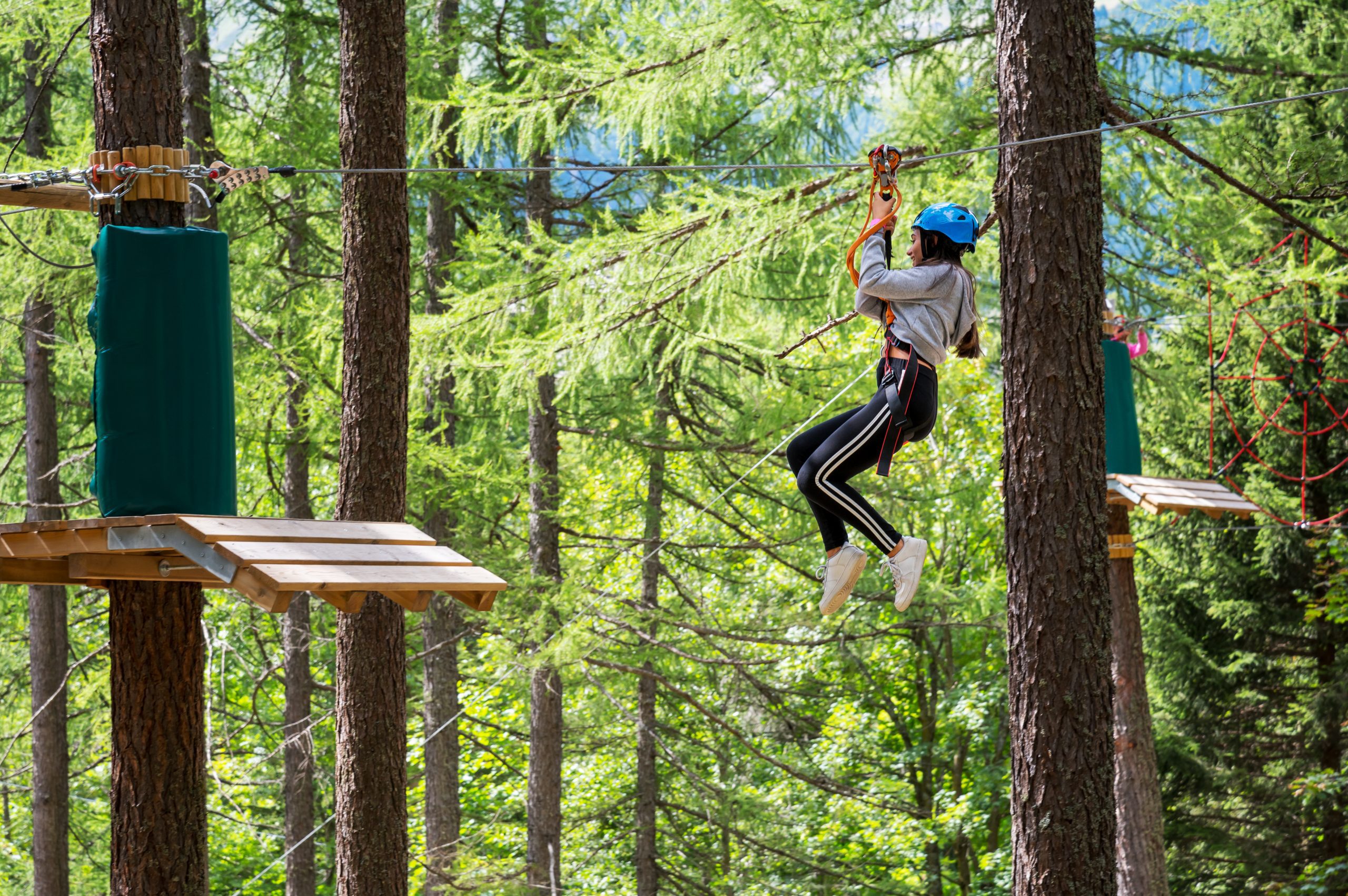 Side view full body of teenager in protective helmet riding on rope while entertaining in green jungle park