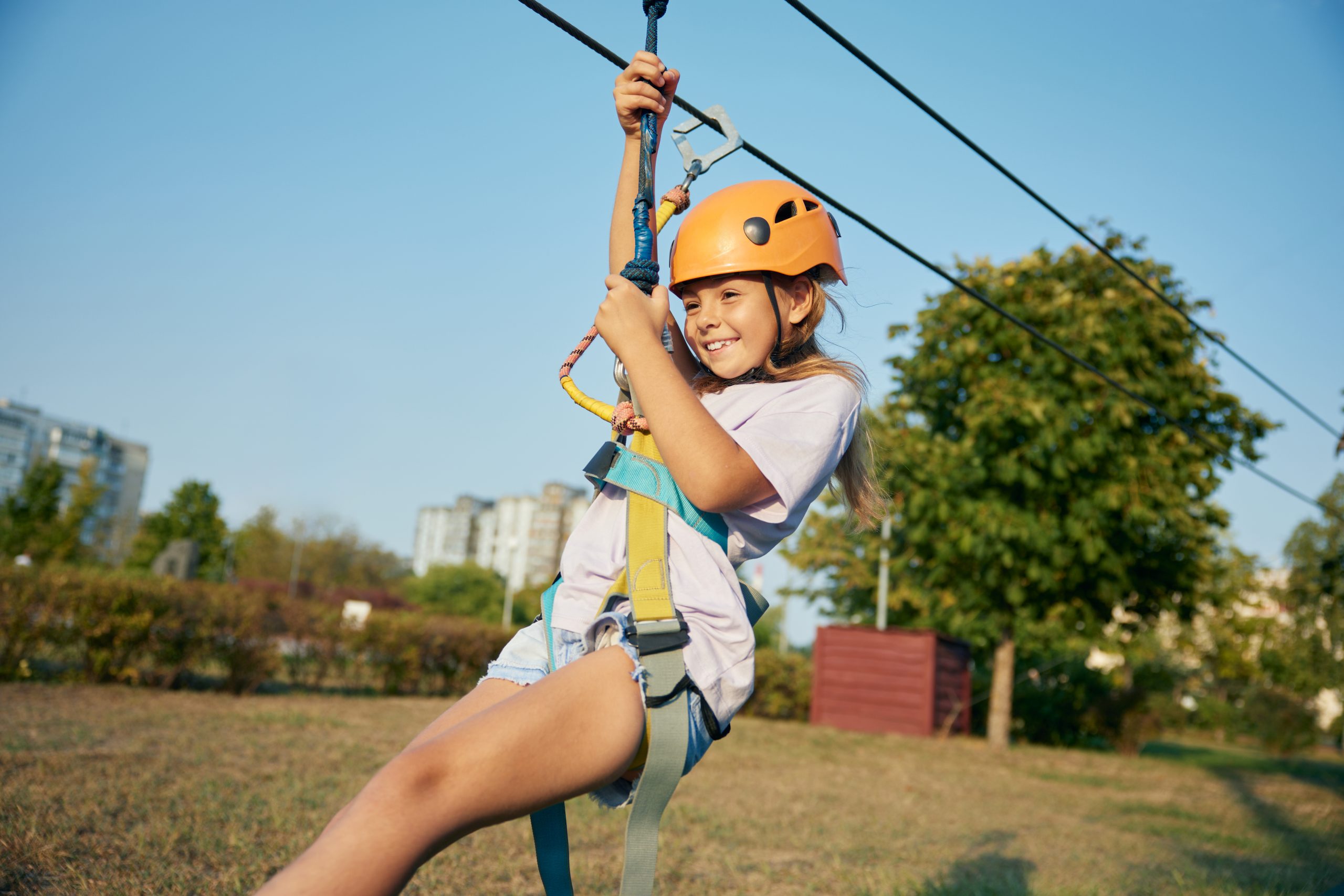 Joyful girl child going down zipline inclined rope with a suspended harness, pulley, or handle. Amusement park for children